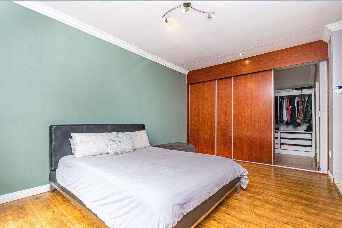 A bedroom featuring wood-look laminate flooring, a sage green accent wall, and built-in wooden sliding-door wardrobes with an integrated walk-in closet area.