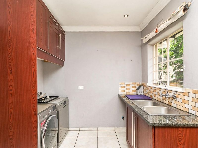 Functional laundry room featuring built-in cabinetry, a double stainless steel sink, tiled splashbacks, and dedicated plumbing connections for appliances.