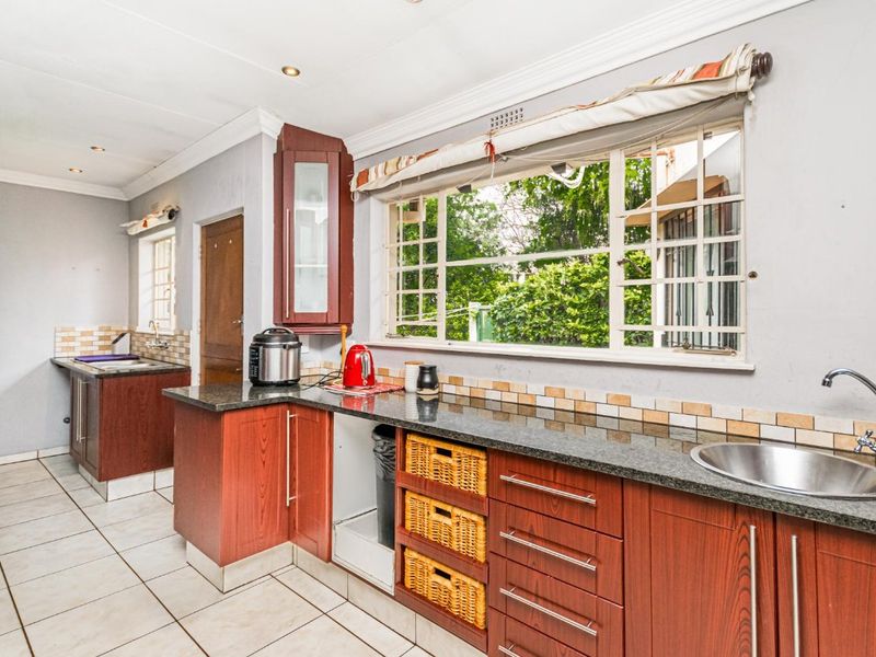 A functional kitchen featuring dark wood cabinetry, granite countertops, tiled flooring, and a large window overlooking the garden.