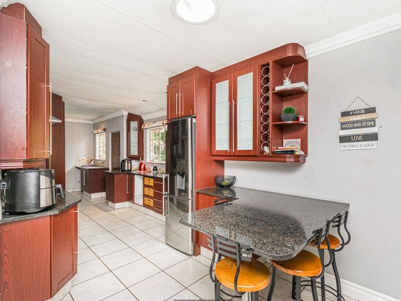 A functional kitchen featuring dark wood cabinetry, granite countertops, a breakfast bar, and tiled flooring, leading into a secondary prep or scullery area.