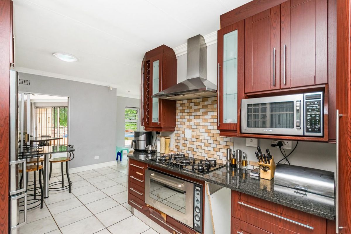 A functional kitchen featuring dark wood cabinetry, granite countertops, a built-in oven, gas hob, and stainless steel extractor fan, with tiled flooring throughout.