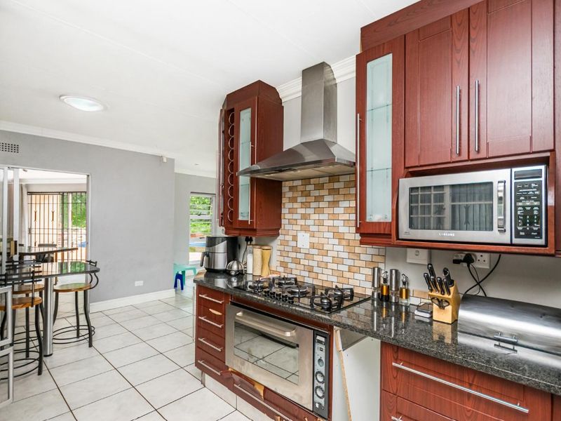 A functional kitchen featuring dark wood cabinetry, granite countertops, a built-in oven, gas hob, and stainless steel extractor fan, with tiled flooring throughout.