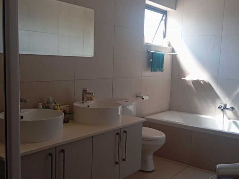 A modern bathroom featuring a double vanity with vessel sinks, a built-in bathtub, and neutral wall tiling.