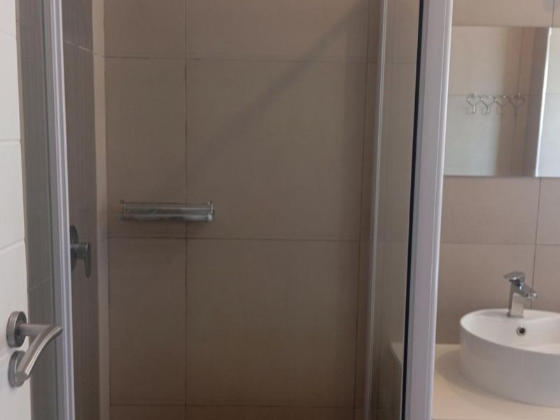 A functional bathroom featuring a walk-in shower enclosure with tiled walls and a modern countertop basin with a chrome faucet.