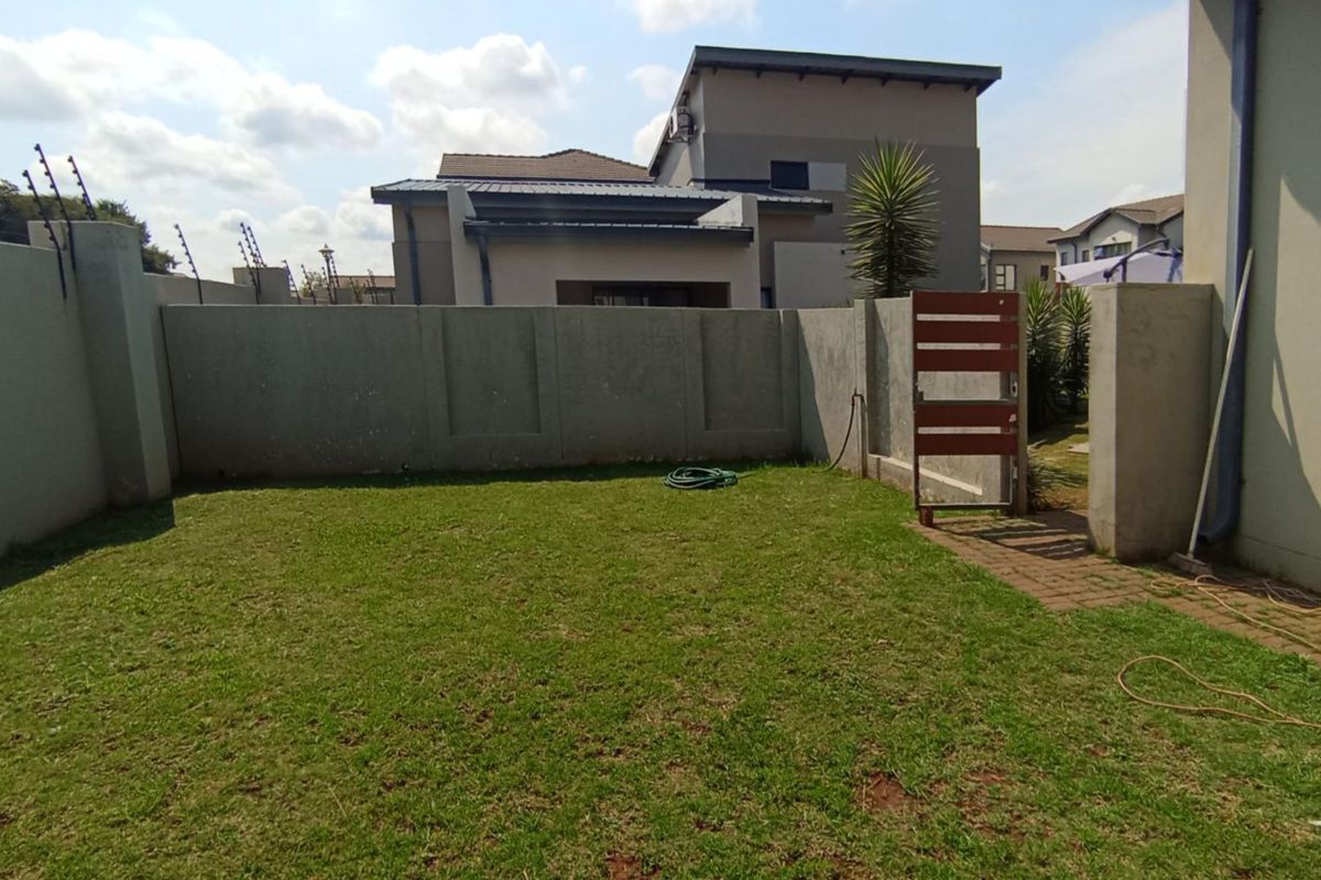 A private rear garden area featuring a manicured lawn, enclosed by high concrete boundary walls with integrated electric fencing.