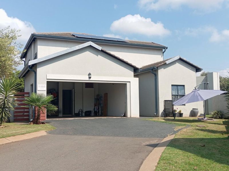 Front elevation of a double-story house featuring a paved driveway, integrated garage, and rooftop solar panels set within a landscaped garden.