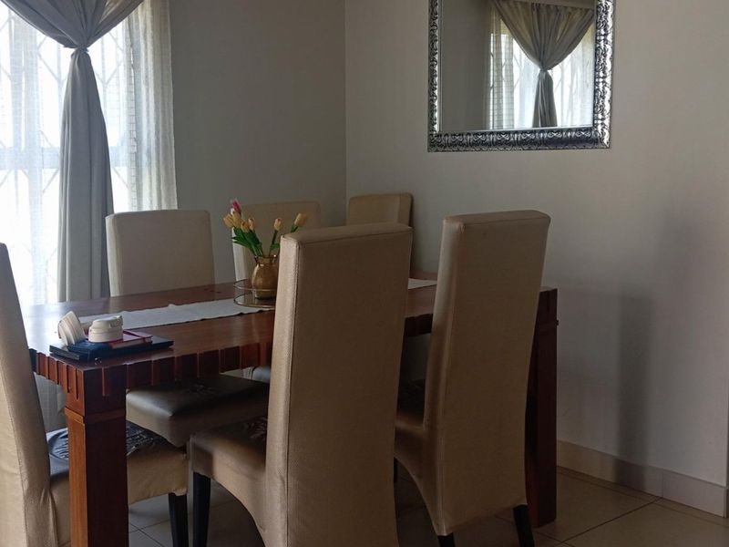 A dining area featuring tiled flooring and a window with security bars, adjacent to a living space.