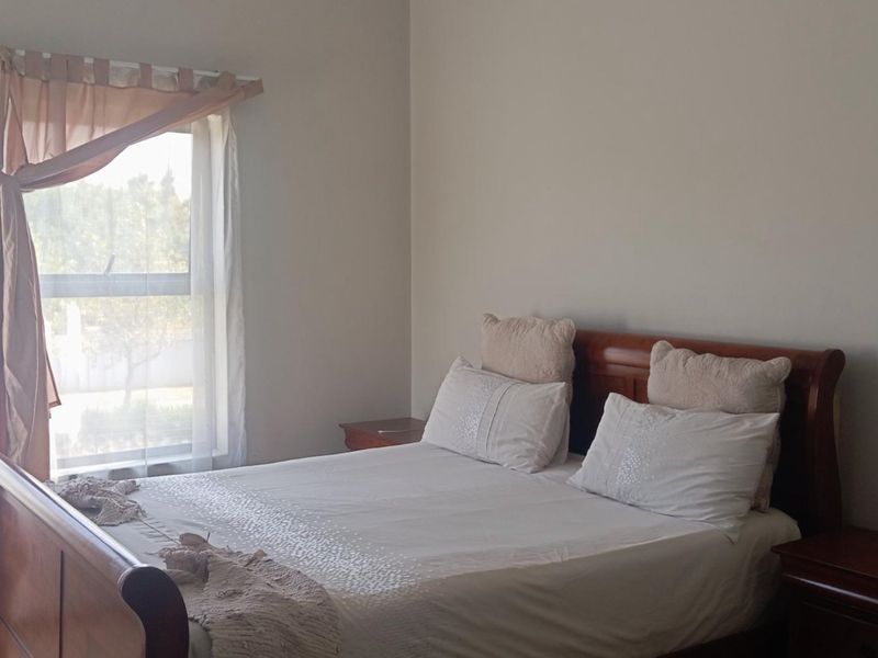 A well-lit bedroom featuring neutral wall tones, a large window with natural light, and ample space for bedroom furniture.