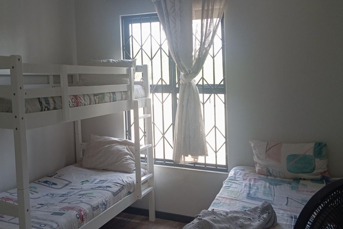 A functional bedroom featuring a window with fitted security bars and laminate flooring.