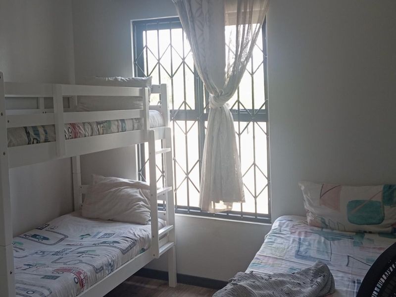 A functional bedroom featuring a window with fitted security bars and laminate flooring.