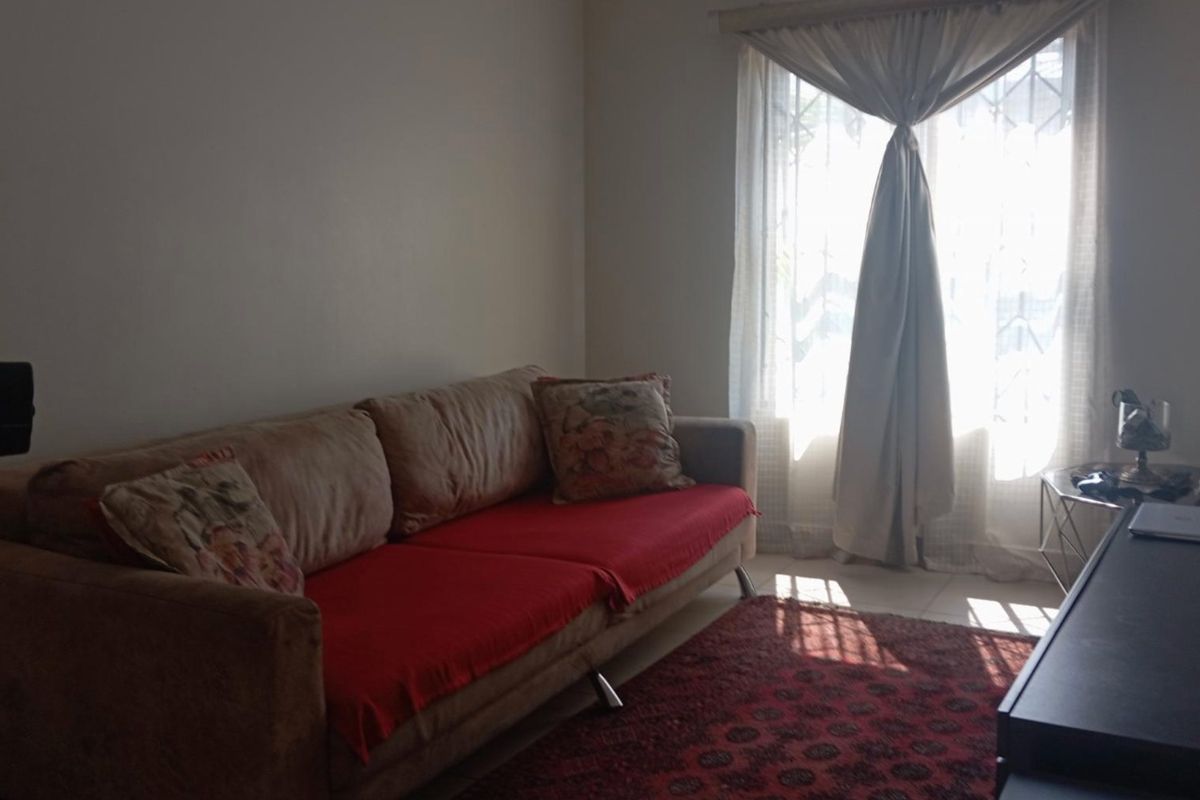A living room featuring tiled flooring and a window with curtains, providing natural light to the space.