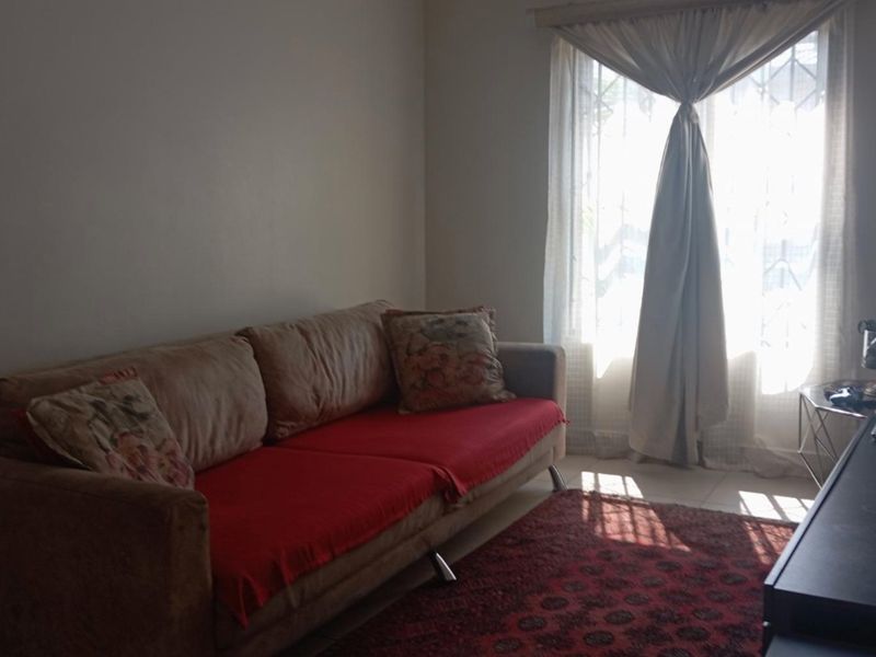 A living room featuring tiled flooring and a window with curtains, providing natural light to the space.