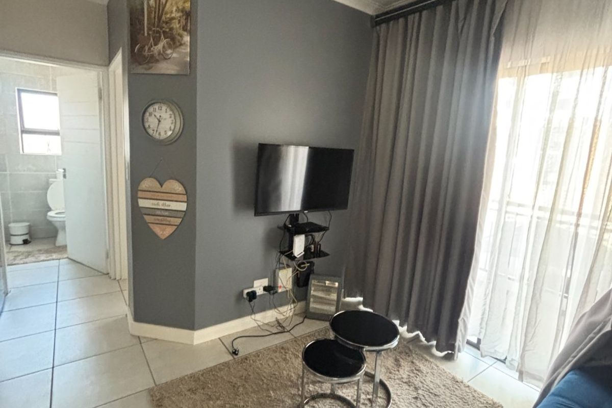 A living room featuring tiled flooring, a feature wall, and sliding door access to a balcony, with an adjacent bathroom visible.
