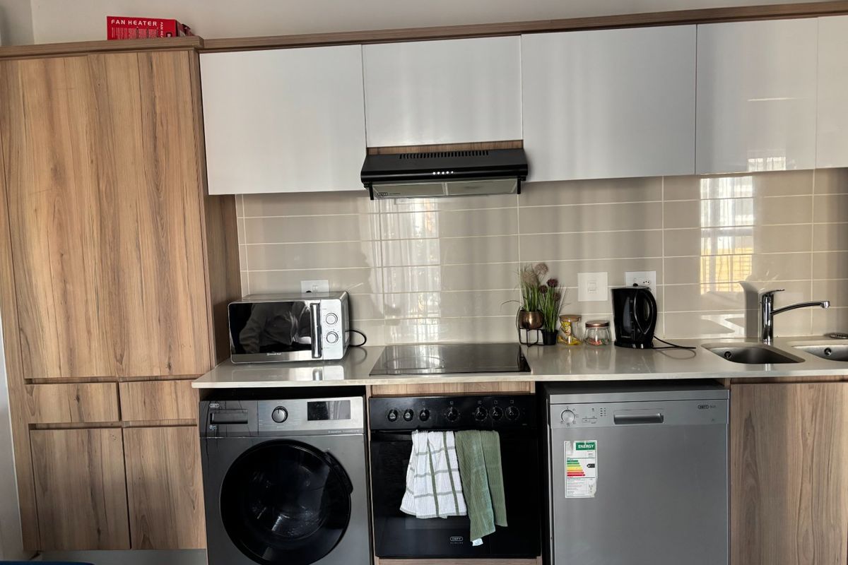 Modern kitchen featuring wood-grain and white cabinetry, integrated oven and hob, extractor fan, tiled backsplash, and dedicated spaces for laundry and dishwasher appliances.