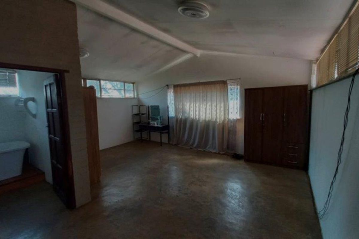 Spacious bedroom featuring concrete flooring, exposed ceiling beams, and an adjoining en-suite bathroom with a bathtub.