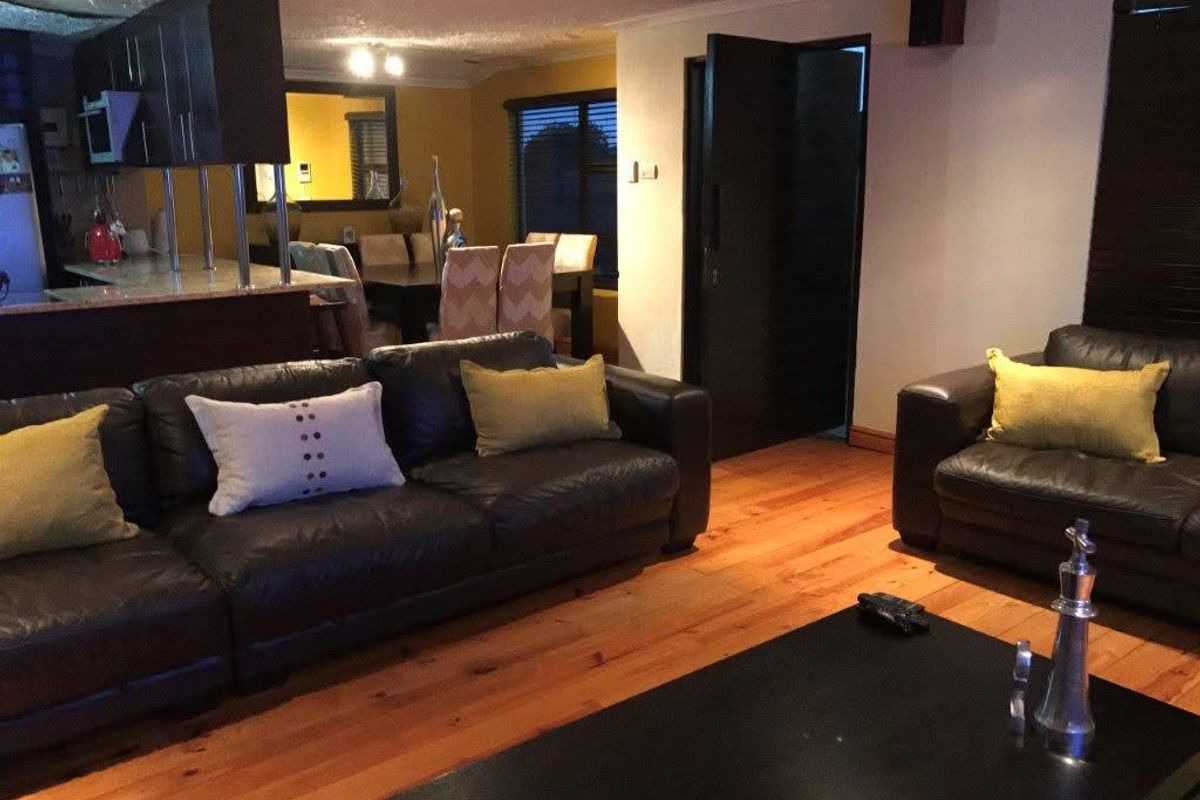 Open plan living and dining area featuring polished timber flooring, dark cabinetry, and integrated kitchen space.