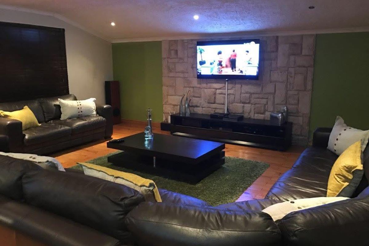 Spacious living room featuring a prominent stone-clad feature wall, recessed downlighting, and polished timber flooring.