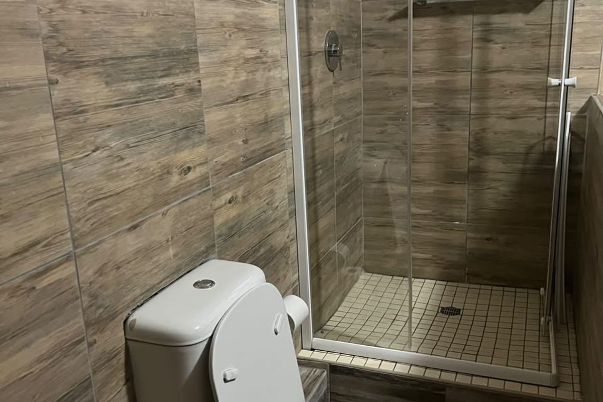 A compact bathroom featuring wood-look wall tiling, a glass-enclosed shower stall, and a modern white toilet.