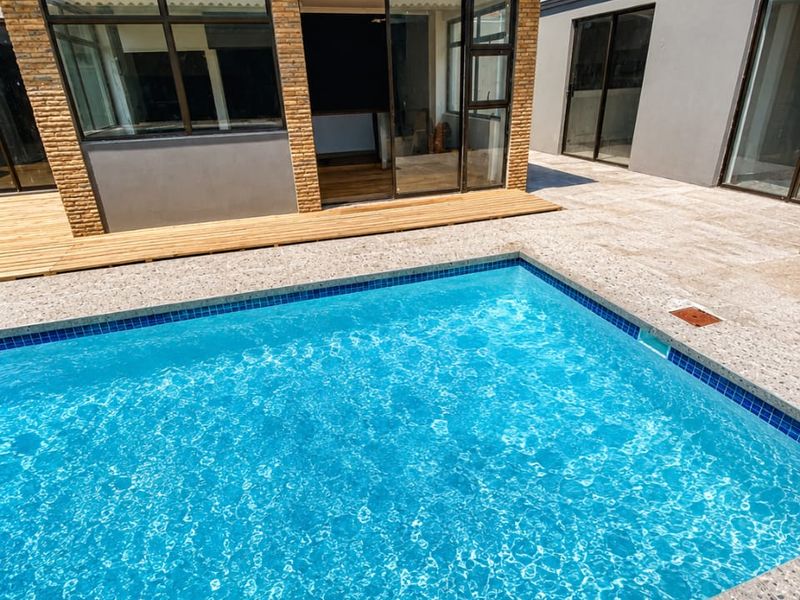 A well-maintained outdoor pool area featuring a tiled surround, wooden decking, and direct access to the home through large sliding glass doors.