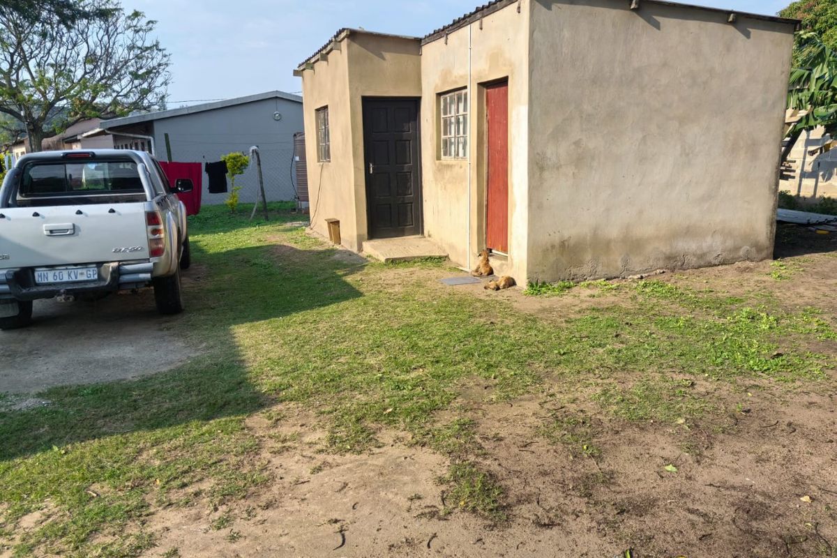 A modest single-story commercial or utility structure featuring a simple plaster finish, dual entry points, and a corrugated roof, situated on a grassed lot.