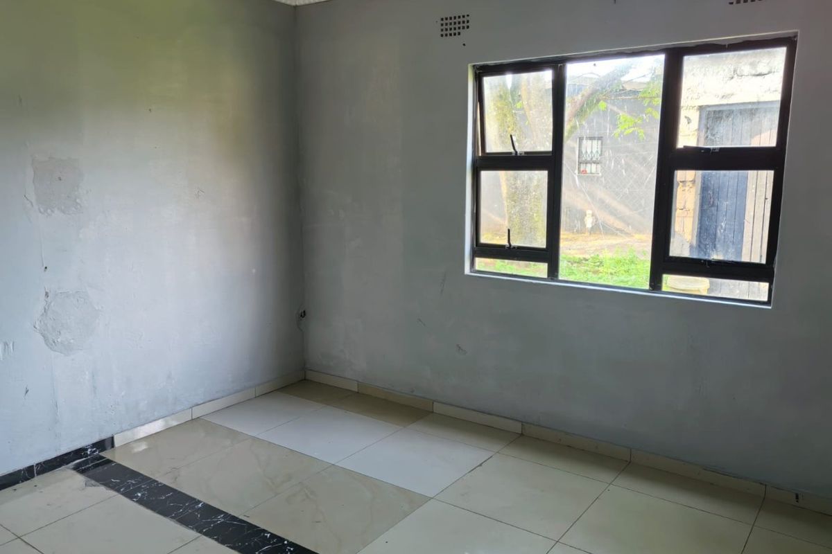An empty room featuring tiled flooring, a large window with metal frames, and visible wall surface imperfections requiring maintenance.