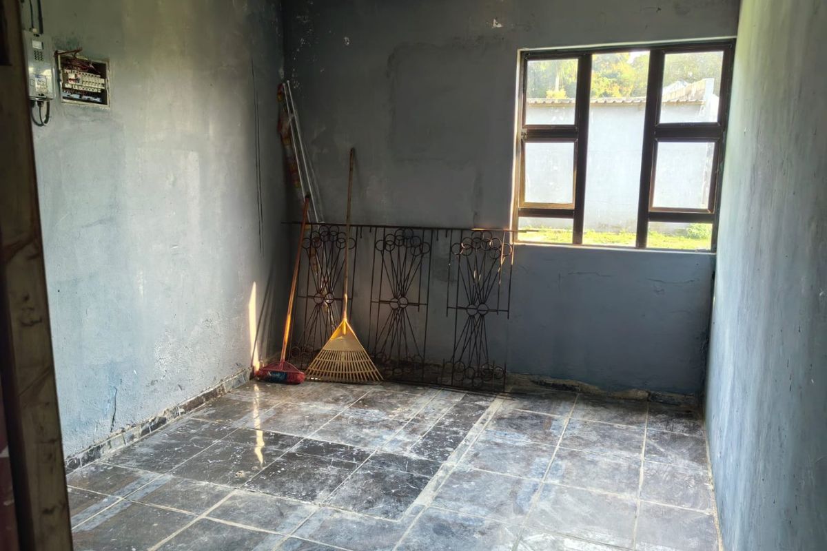 An empty room featuring dark tiled flooring and grey walls, with a window providing natural light. Suitable for renovation or repurposing.
