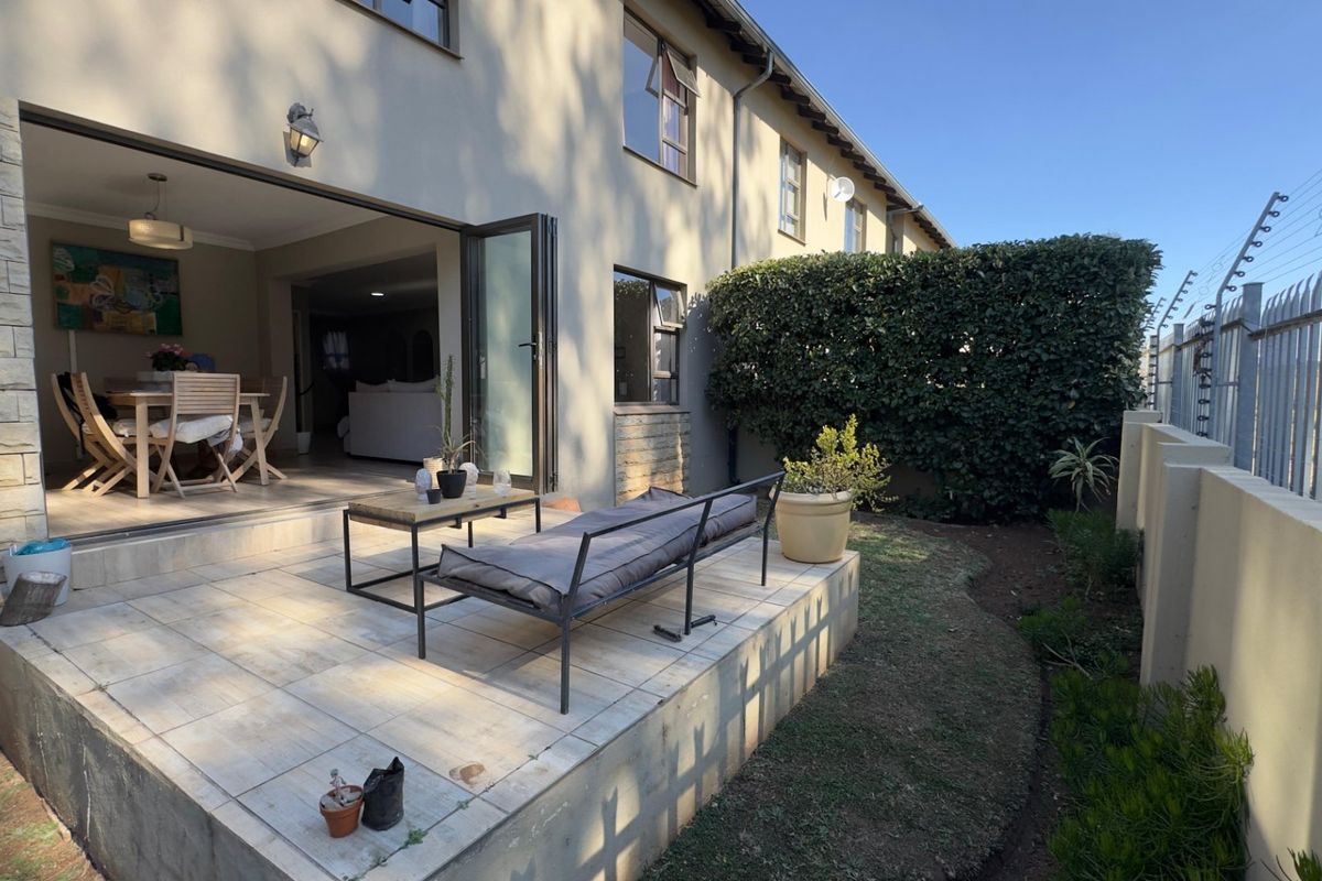 A rear patio area featuring tiled flooring and seamless access to the interior living space, complemented by a private garden and perimeter security fencing.