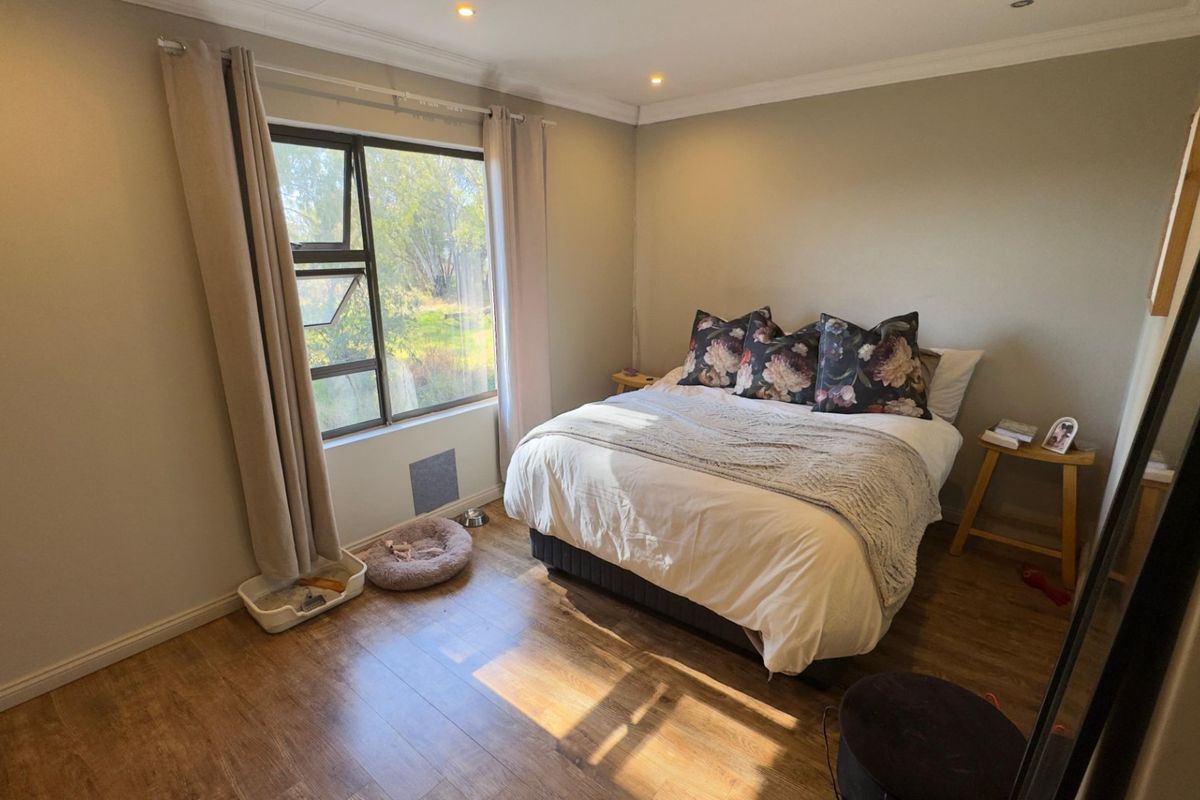 A well-lit bedroom featuring wood-look flooring, neutral wall tones, and a large window providing natural light and garden views.