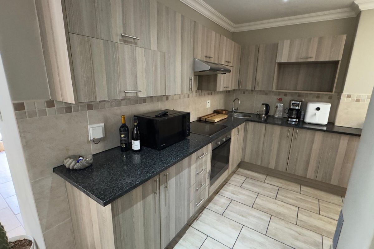 A functional kitchen featuring wood-grain cabinetry, dark granite countertops, a built-in oven, extractor fan, and tiled flooring.