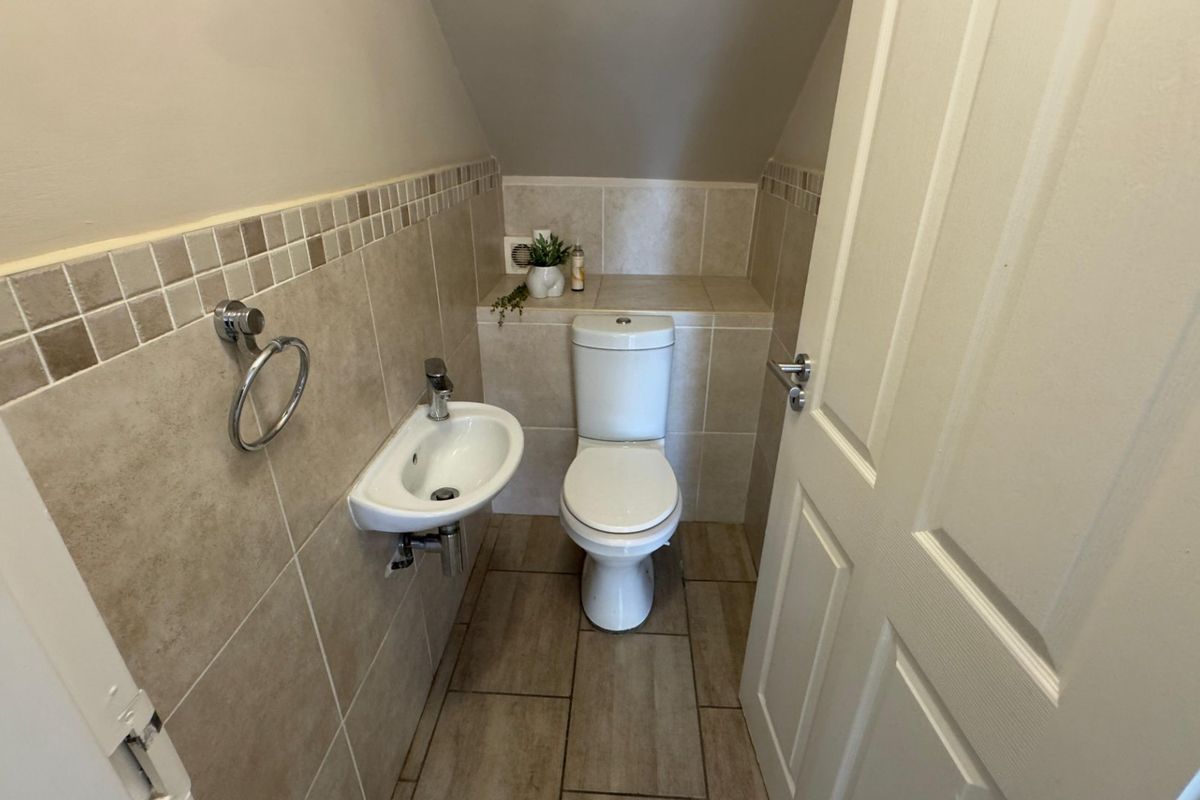 A compact guest cloakroom featuring a wall-mounted basin, a modern toilet, and neutral tiled walls with a decorative mosaic border.