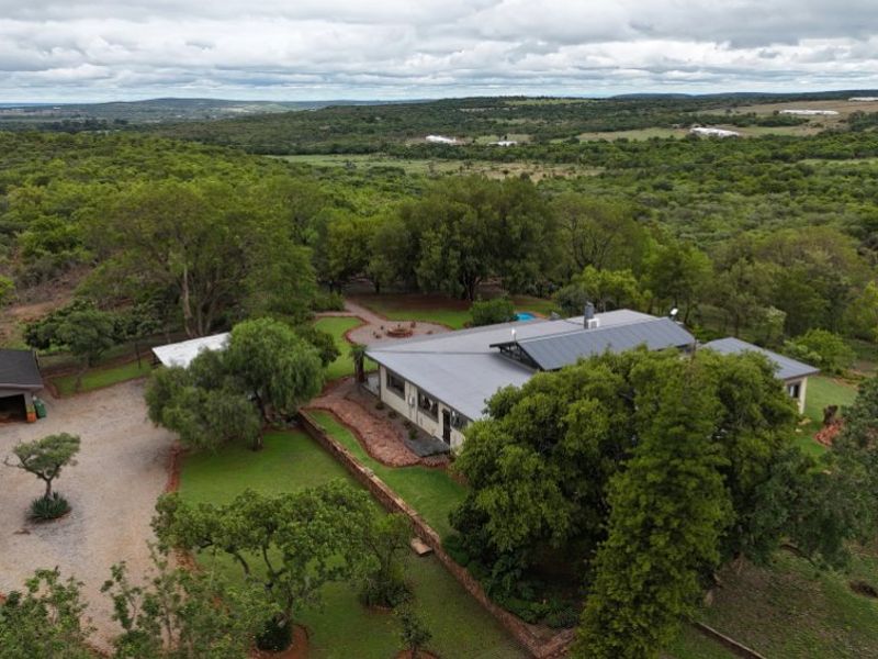Aerial view of a farm property featuring a main residence, detached garage, landscaped gardens, and expansive surrounding natural landscape.