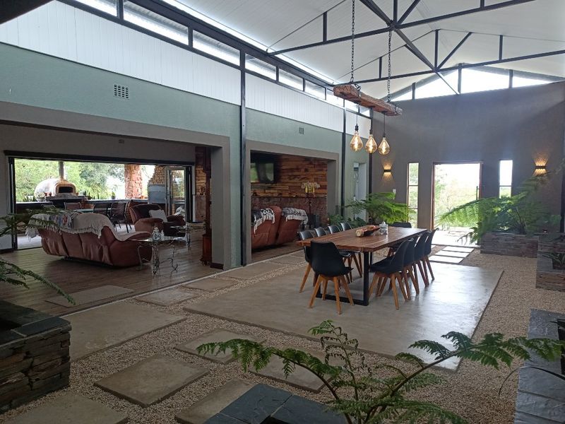 Spacious open-plan living and dining area featuring high vaulted ceilings, exposed steel trusses, polished concrete flooring, and seamless indoor-outdoor flow to a covered patio.