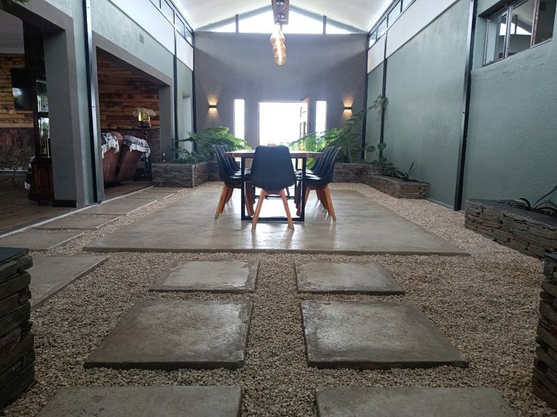 A unique indoor-outdoor dining area featuring a central concrete platform, stone-clad planters, and high vaulted ceilings with exposed structural beams.