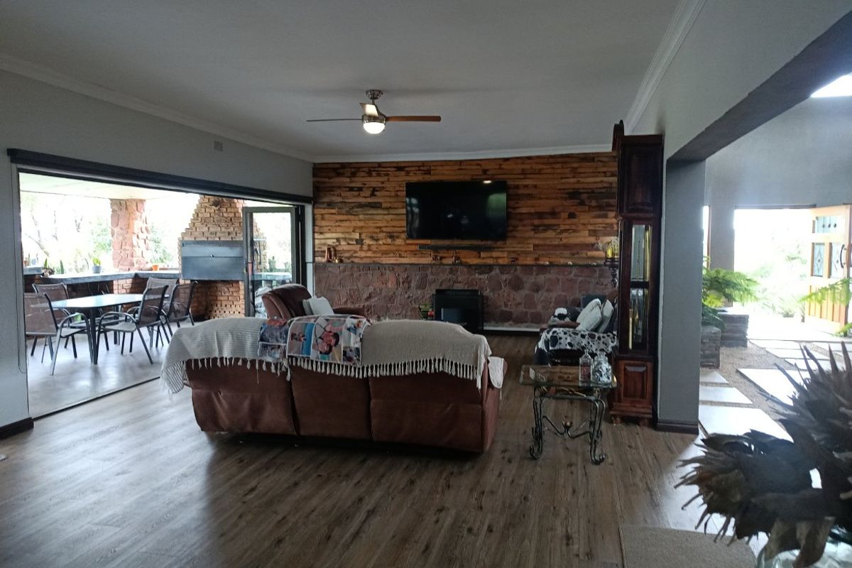 Spacious living room featuring a rustic stone and timber-clad feature wall, wood-look flooring, and seamless flow to an outdoor patio area.