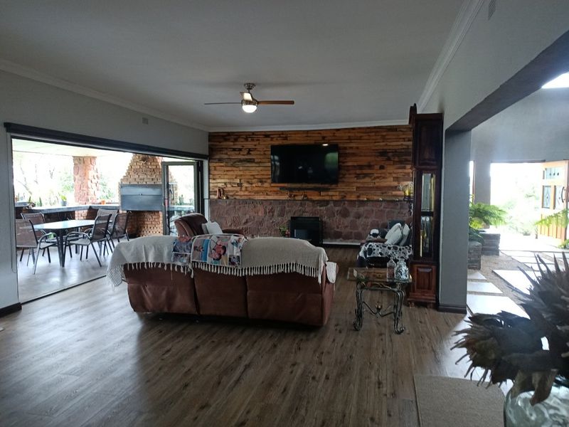 Spacious living room featuring a rustic stone and timber-clad feature wall, wood-look flooring, and seamless flow to an outdoor patio area.