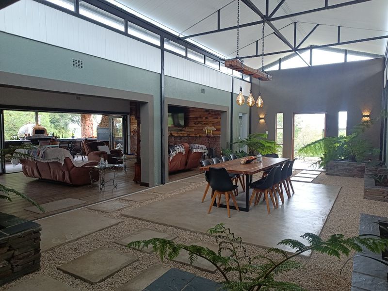Spacious open-plan living and dining area featuring high vaulted ceilings, exposed steel trusses, polished concrete flooring, and seamless indoor-outdoor flow to a covered patio.
