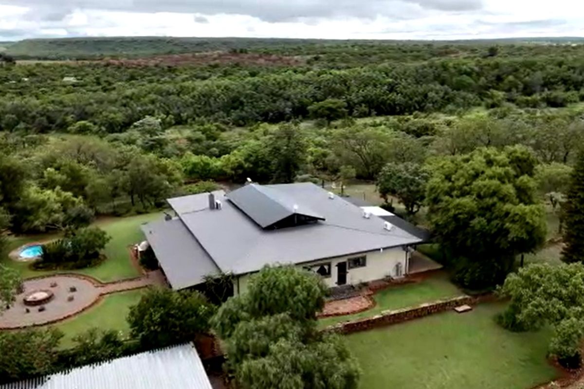 Aerial view of a farm property featuring a large residence with a metal roof, a swimming pool, and expansive landscaped grounds.