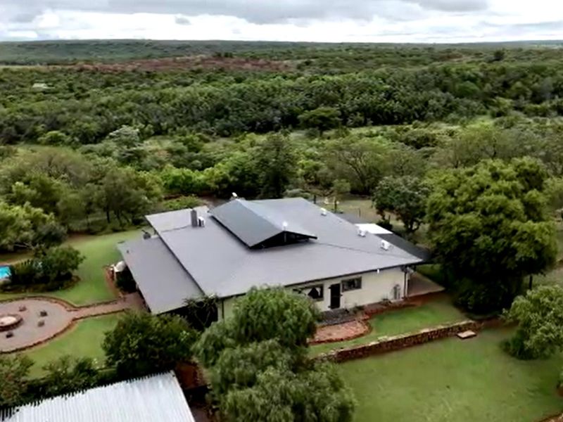 Aerial view of a farm property featuring a large residence with a metal roof, a swimming pool, and expansive landscaped grounds.