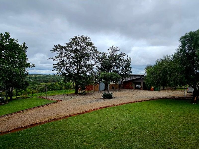 A wide view of the farm property featuring a gravel driveway, expansive lawn, mature trees, and the main building structure in the background.