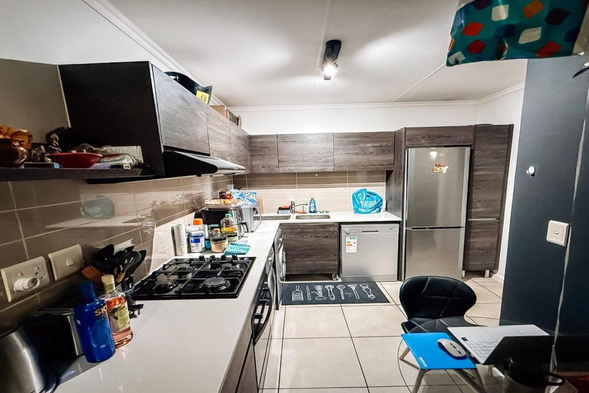 A functional kitchen featuring dark wood-grain cabinetry, tiled splashbacks, a gas hob, extractor fan, and integrated space for a dishwasher and refrigerator.
