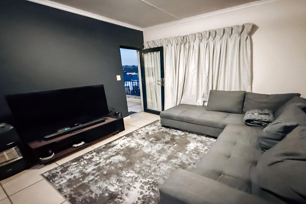 A living room featuring tiled flooring, a dark accent wall, and a glass door providing access to an outdoor balcony area.