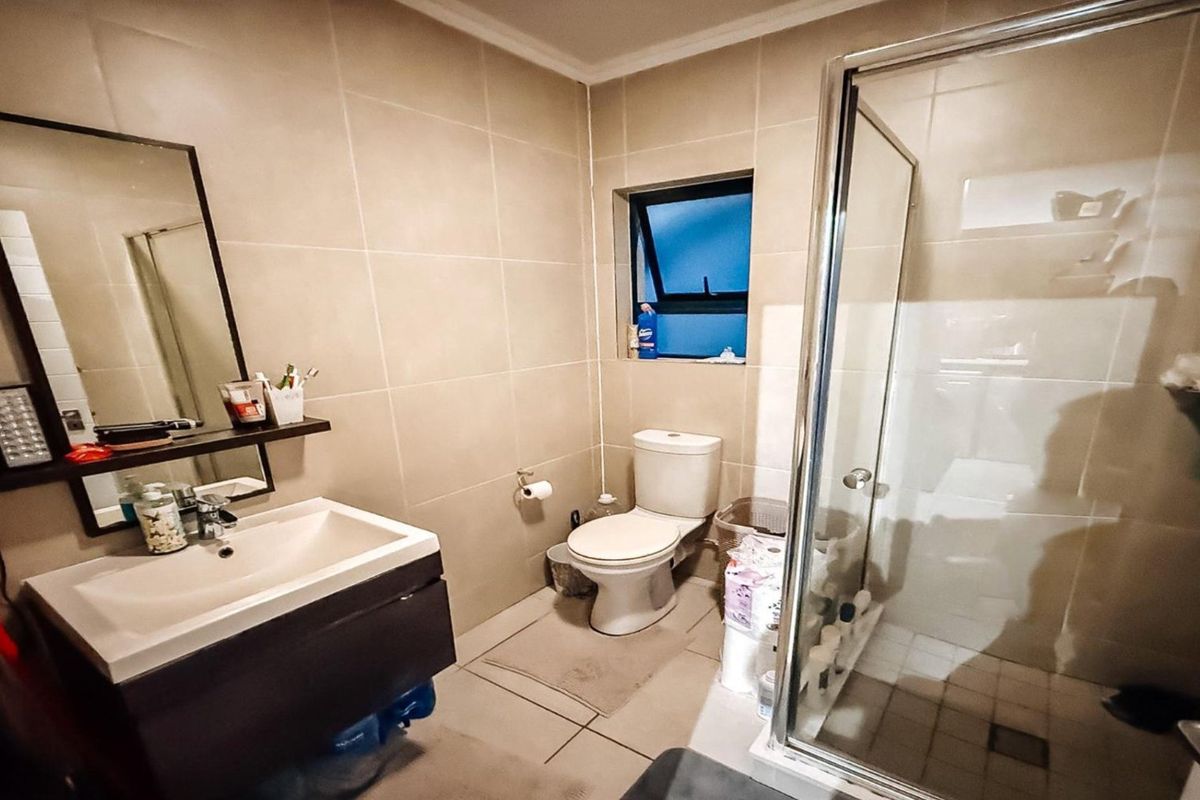 A functional bathroom featuring a glass-enclosed shower, a modern vanity with basin, and a standard toilet with neutral wall tiling.