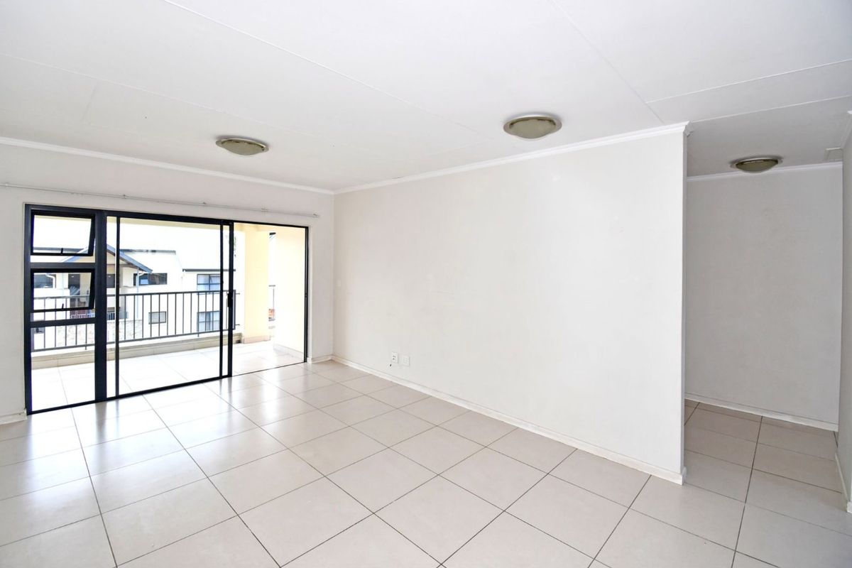 An open-plan living area featuring neutral floor tiles, flush-mount ceiling lights, and large sliding glass doors leading to a private balcony.