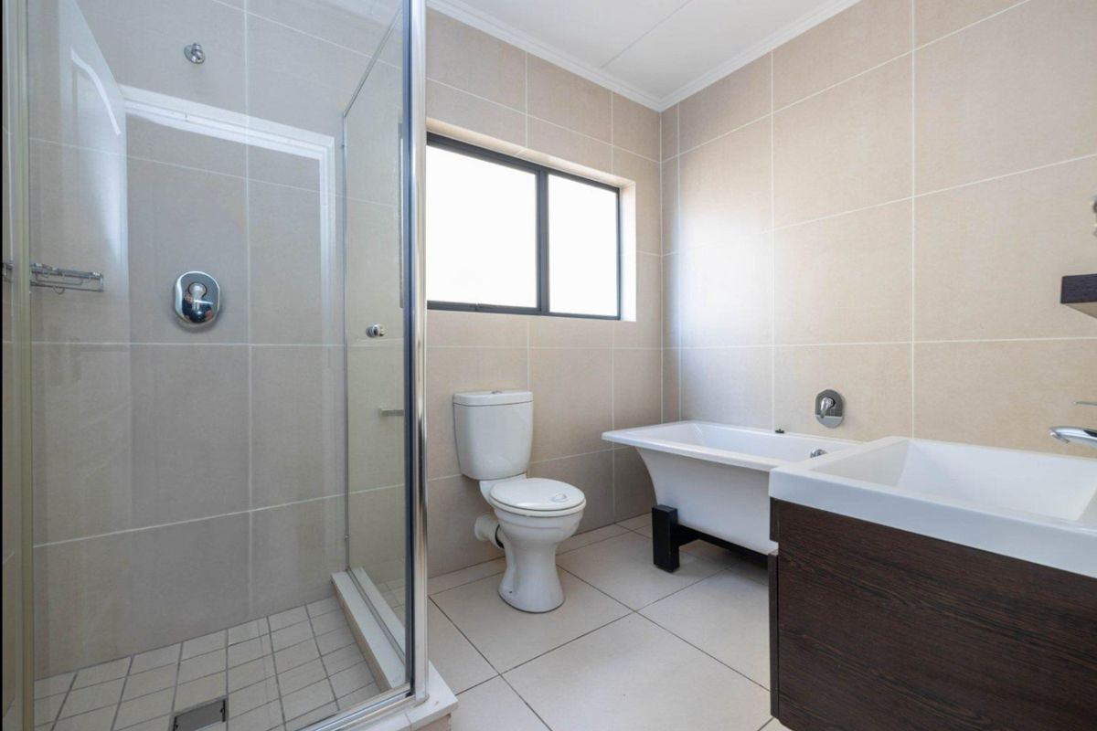 Modern bathroom featuring a glass-enclosed shower, a freestanding bathtub, a wall-mounted toilet, and a vanity unit with neutral floor-to-ceiling tiling.
