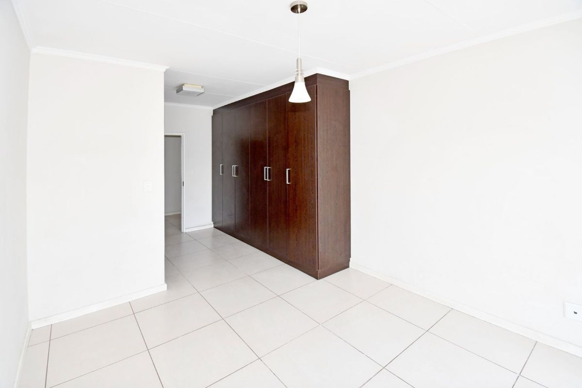 A bright, empty bedroom featuring neutral floor tiles, white walls, and a large, dark wood built-in wardrobe with modern hardware.