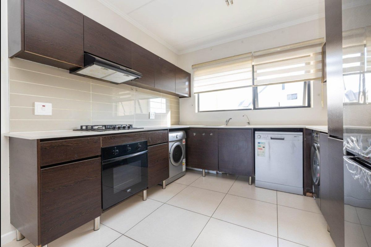 A functional kitchen featuring dark wood cabinetry, tiled flooring, a built-in oven, gas hob, extractor fan, and integrated space for laundry appliances.