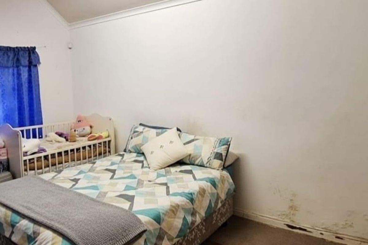 A bedroom featuring a vaulted ceiling and carpeted flooring, currently showing signs of moisture damage on the lower wall section.