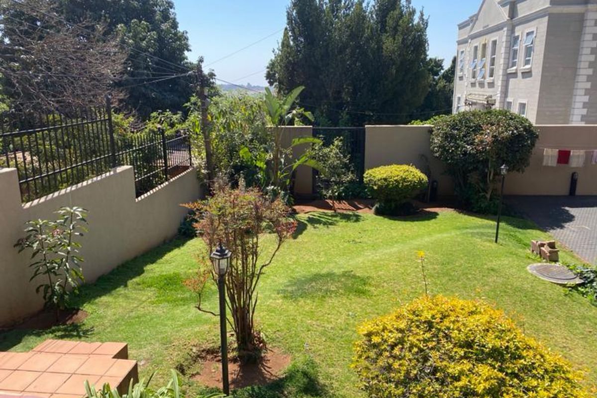 A well-maintained private rear garden featuring a manicured lawn, established shrubs, perimeter boundary walls, and a paved driveway area.