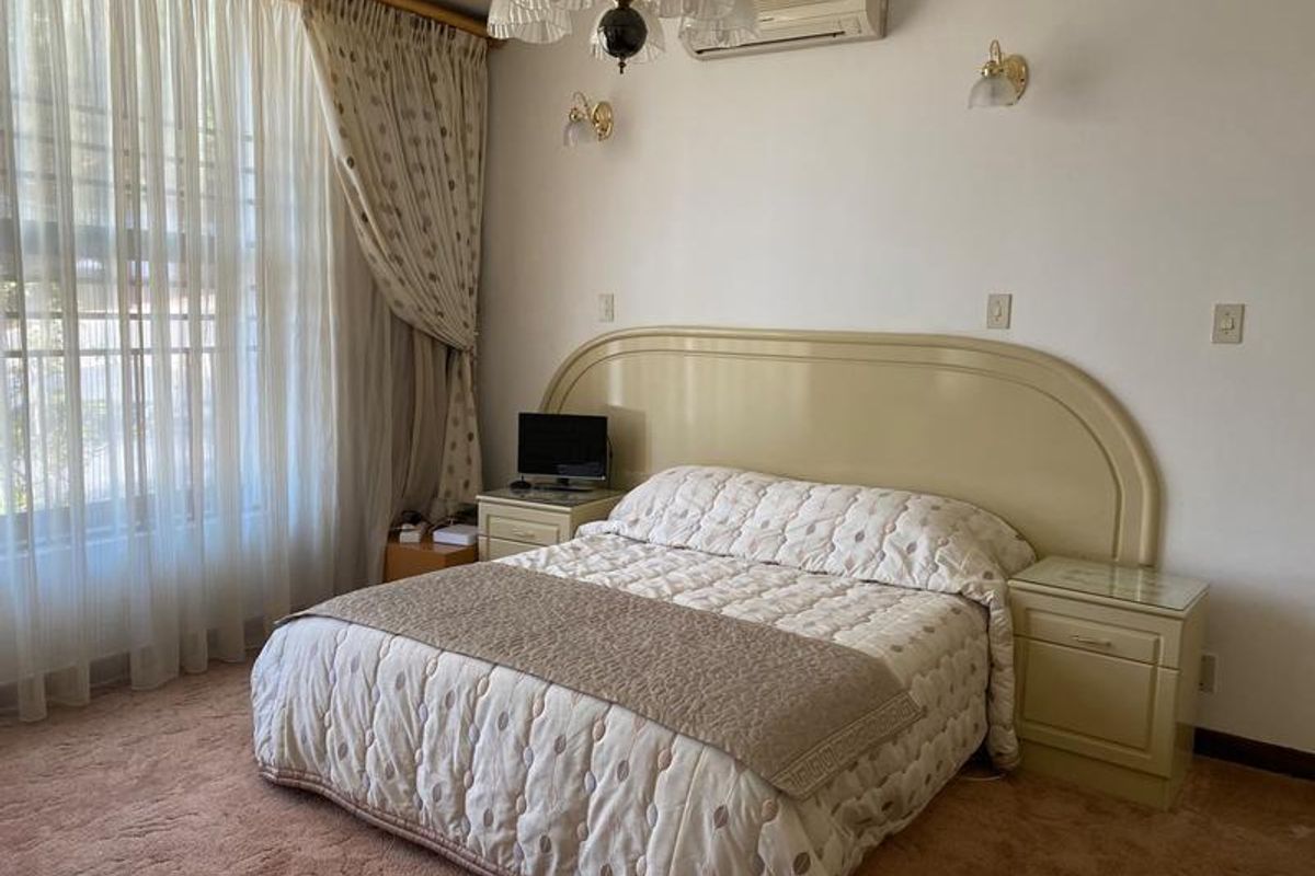 A spacious bedroom featuring a built-in headboard, wall-mounted air conditioning unit, and large windows with floor-to-ceiling curtains.