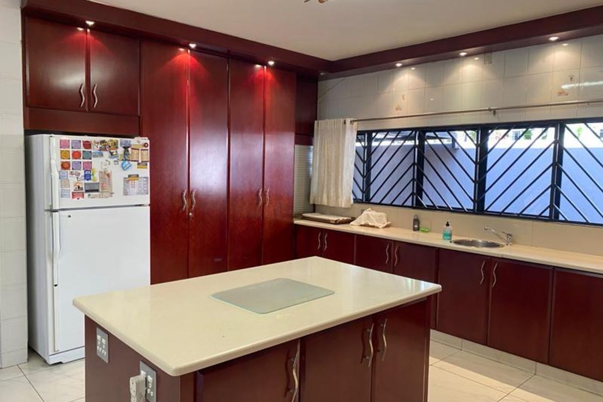 A spacious kitchen featuring dark wood cabinetry, a central island with a stone countertop, and large windows with security bars.